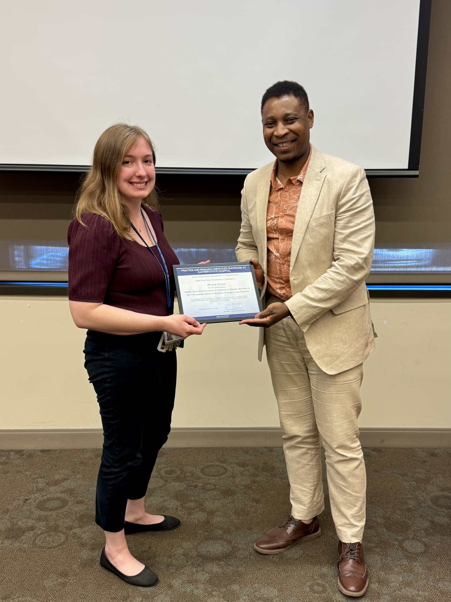 Early career woman receiving award from mid career man in light suit