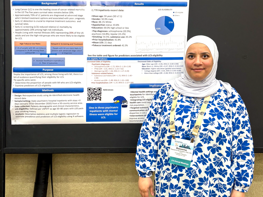 woman in blue floral dress and white hijab with research poster behind her