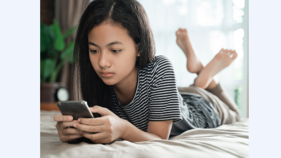 teenage girl laying on her bed on her phone